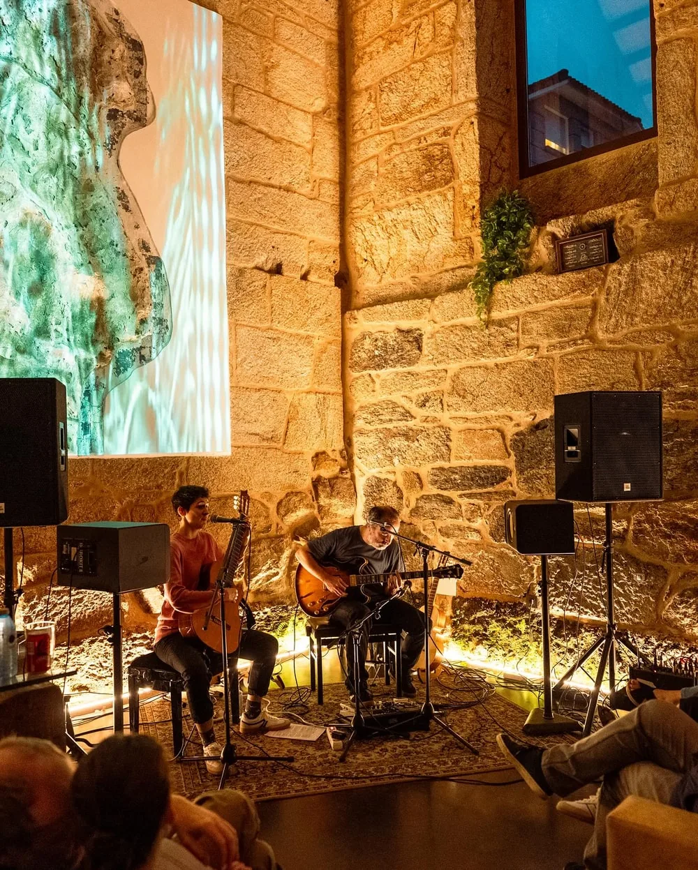 Dúo de guitarra actuando junto a la pared de piedra iluminada en tonos cálidos