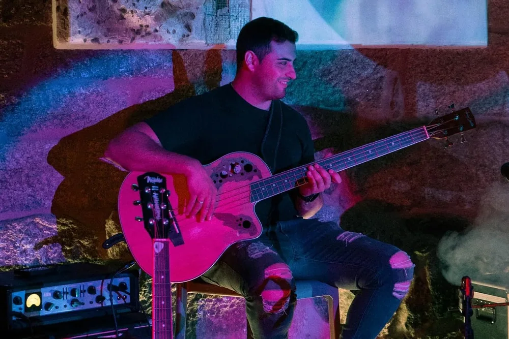 Bajista sonriendo durante un concierto, iluminado con luz rosa y humo de escena