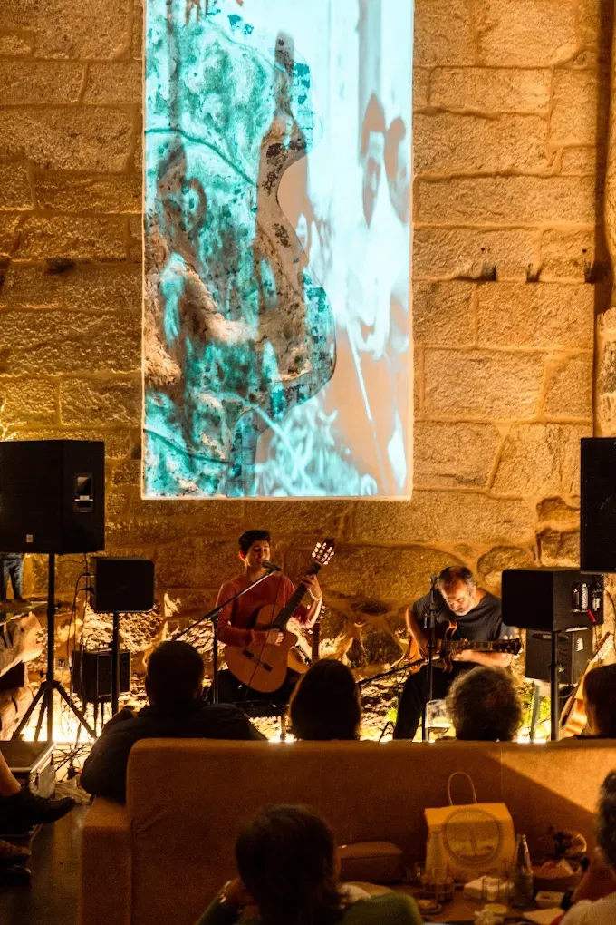 El salón de noche durante un concierto, con una proyección iluminada sobre el muro y el público en los sofás