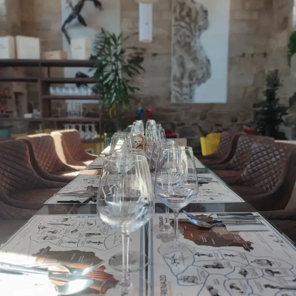 Mesa preparada con copas de vino y manteles ilustrados con el mapa de As Neves